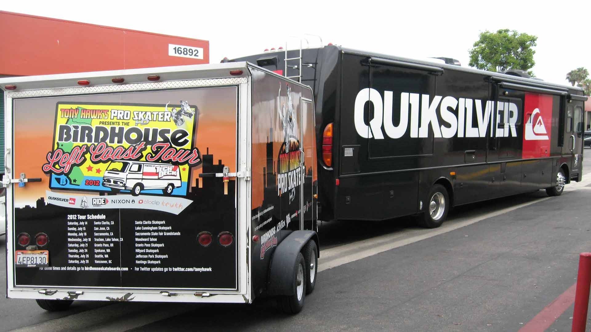 A black Quiksilver bus towing a trailer with a Birdhouse 