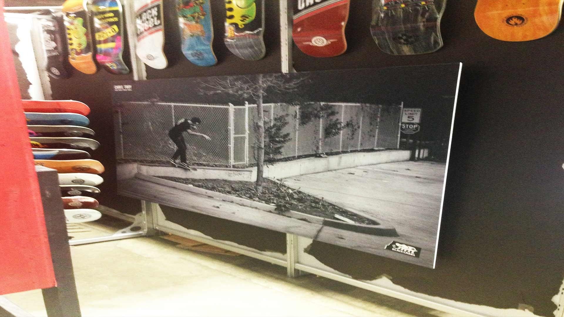 A black-and-white print of a skateboarder grinding a ledge, displayed on a wall with rows of skateboard decks above.