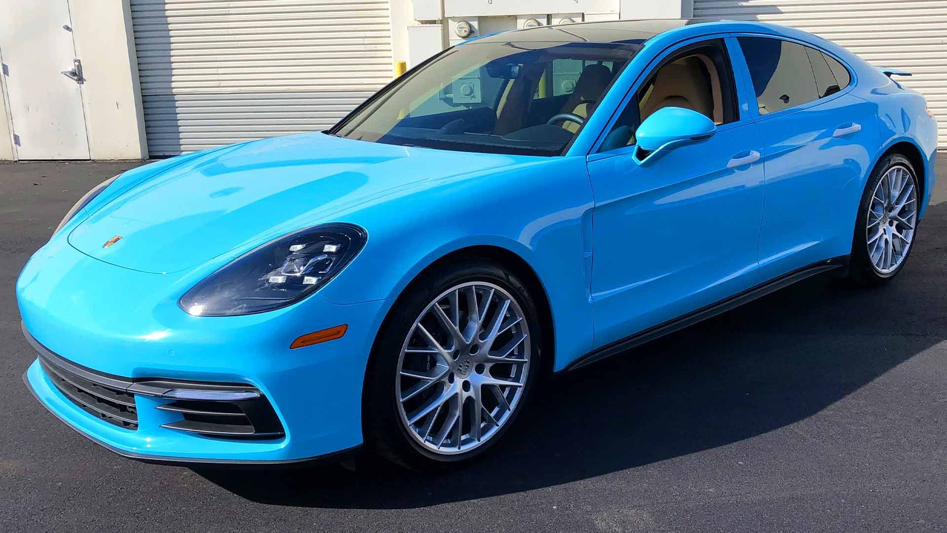 A bright blue Porsche Panamera sedan parked on an asphalt surface in front of a white garage door.