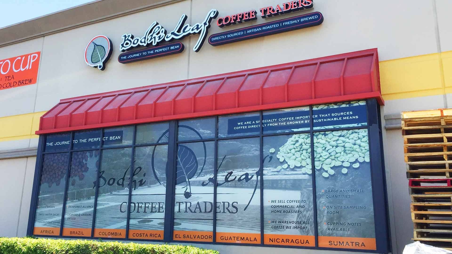 The storefront of Bodhi Leaf Coffee Traders, featuring large glass windows, a red awning, and a cream-colored exterior.