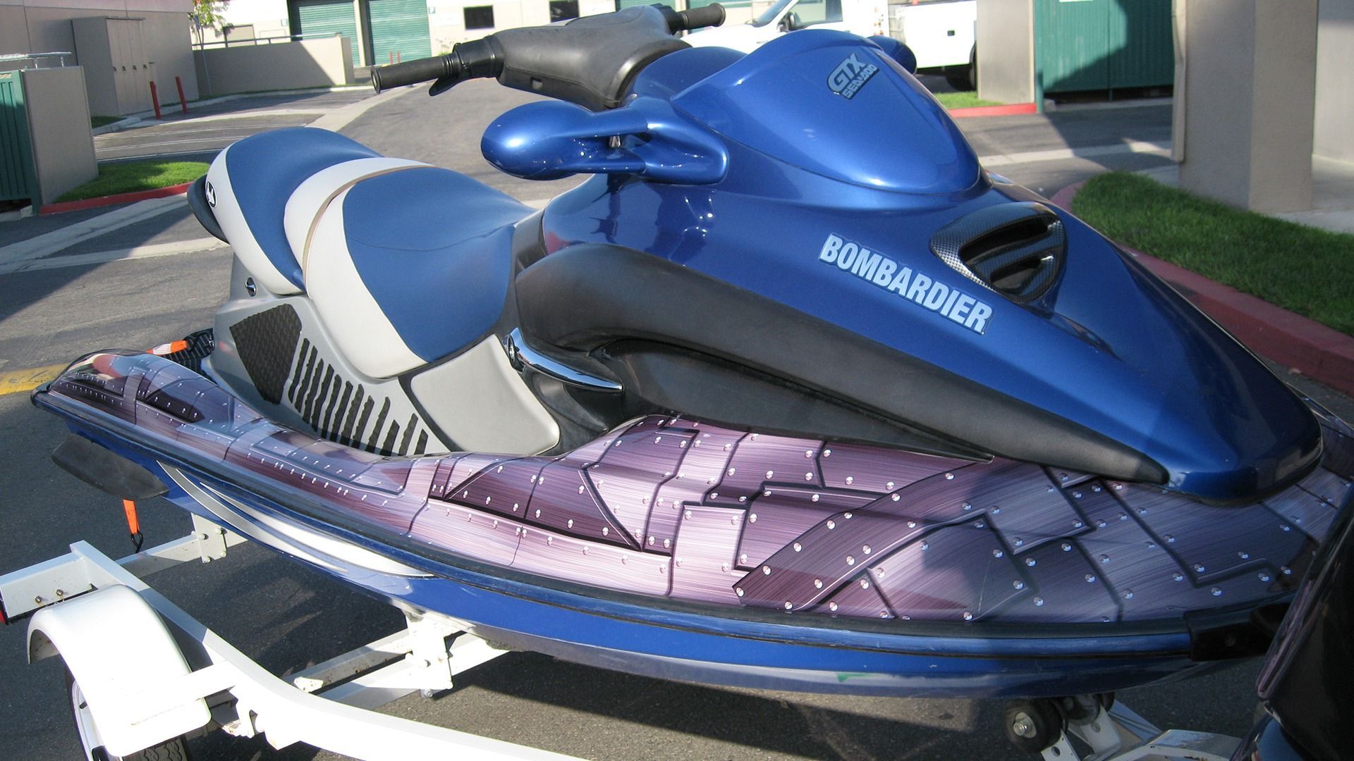 A blue Bombardier personal watercraft on a trailer with a unique purple, geometric-patterned graphic on its hull.