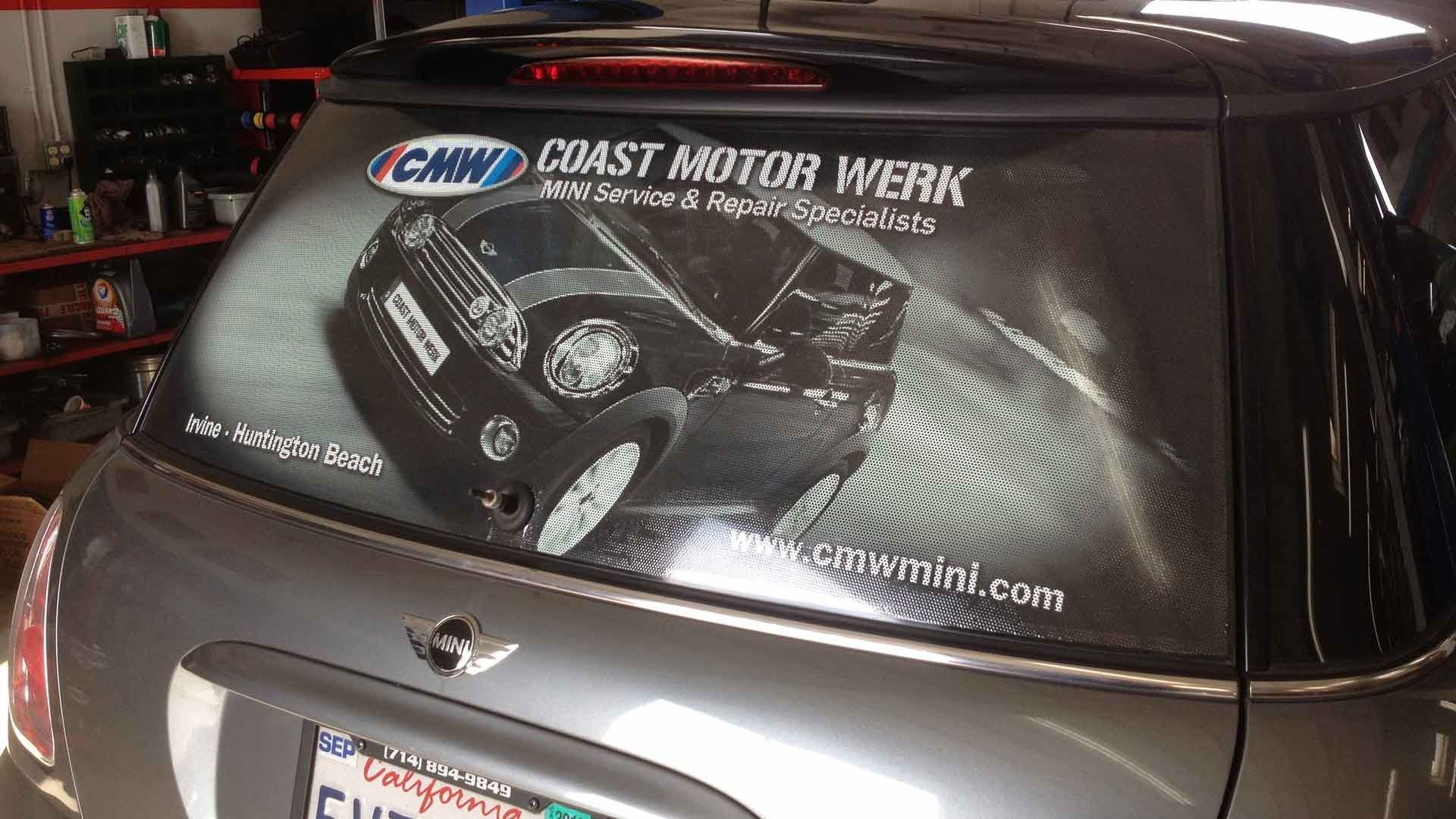 Rear view of a grey Mini Cooper with a branded perforated window decal for Coast Motor Werk advertising MINI services.