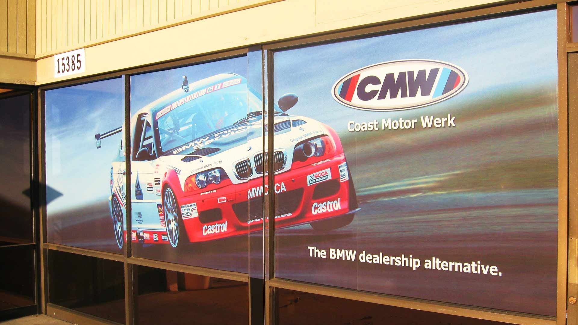 Storefront window graphic for CMW, featuring a red and white BMW race car and the text 