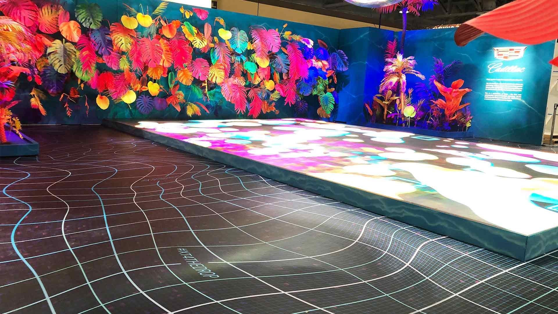 A vibrant display stage featuring a wall of colorful artificial flowers, a light-up floor, and a grid-patterned carpet.