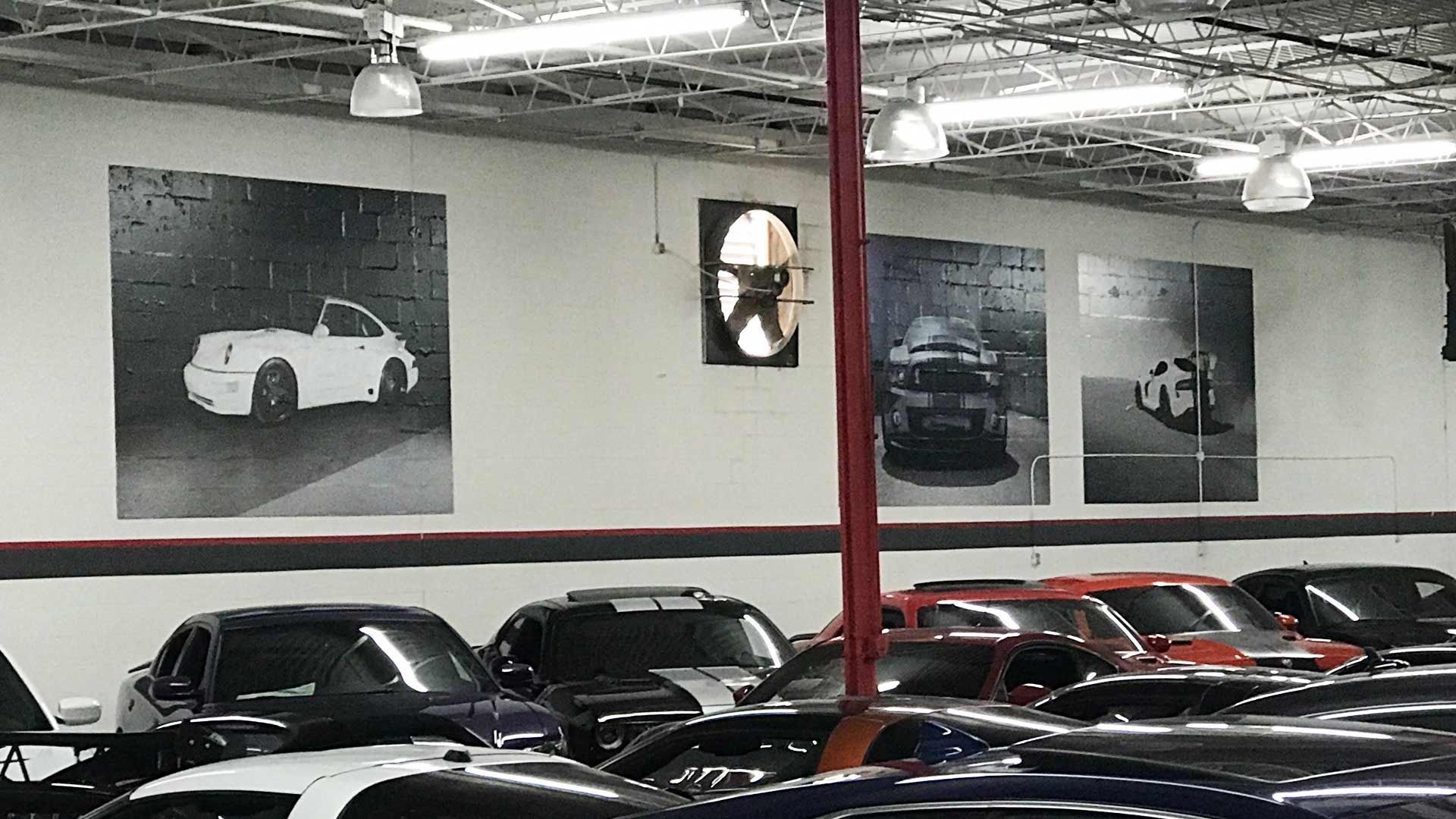 A warehouse showroom displaying several vehicles beneath three large black-and-white posters of cars on a white wall.