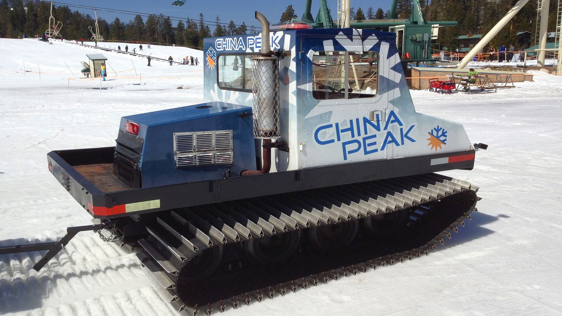 A China Peak snow groomer with blue and silver branding sits on a snowy slope with a ski lift in the background.