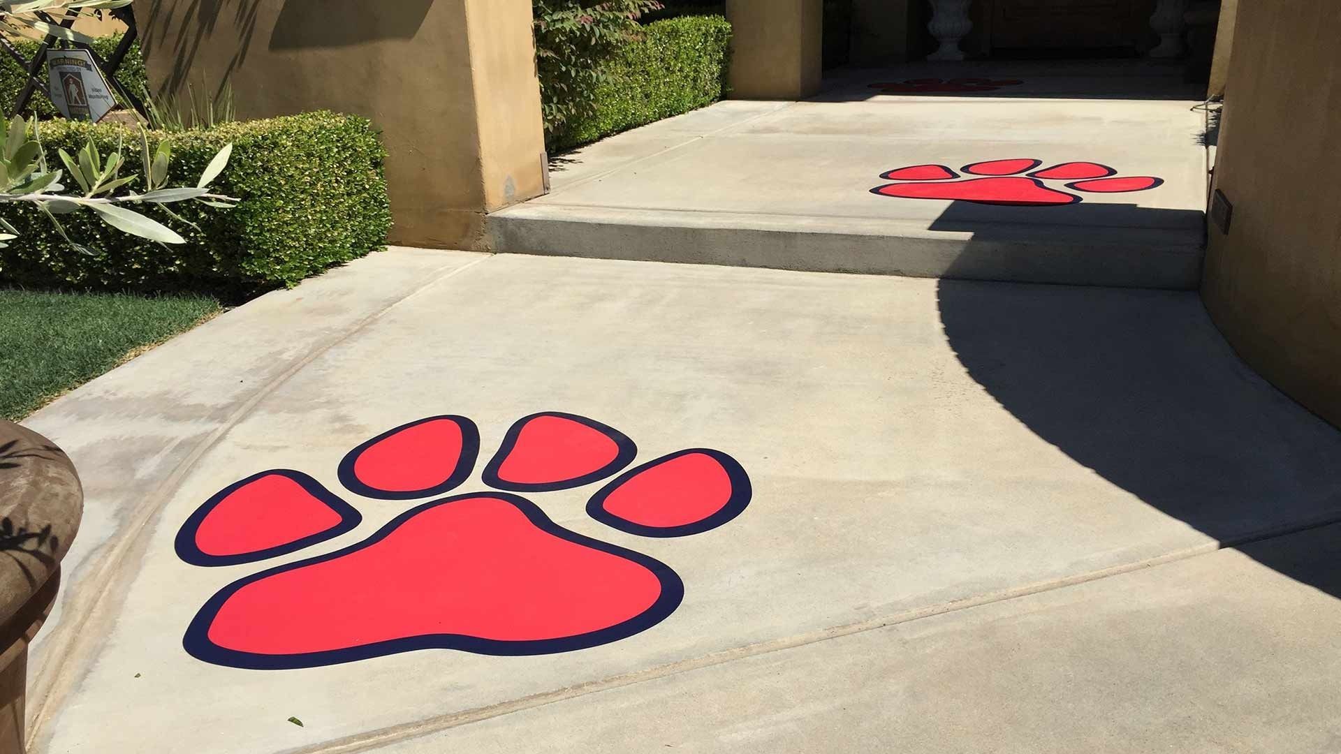 Two large red, cartoon-style paw prints are painted on a concrete walkway leading up to a residential entrance.