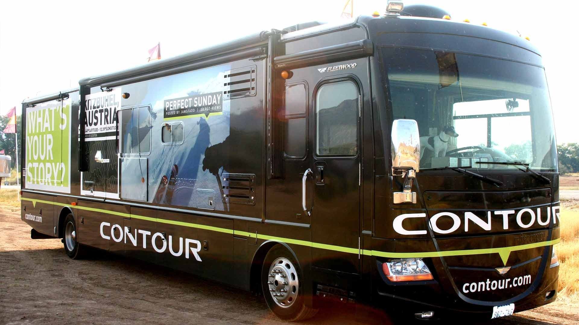 A black Contour-branded motorcoach parked on a dirt lot, featuring a 