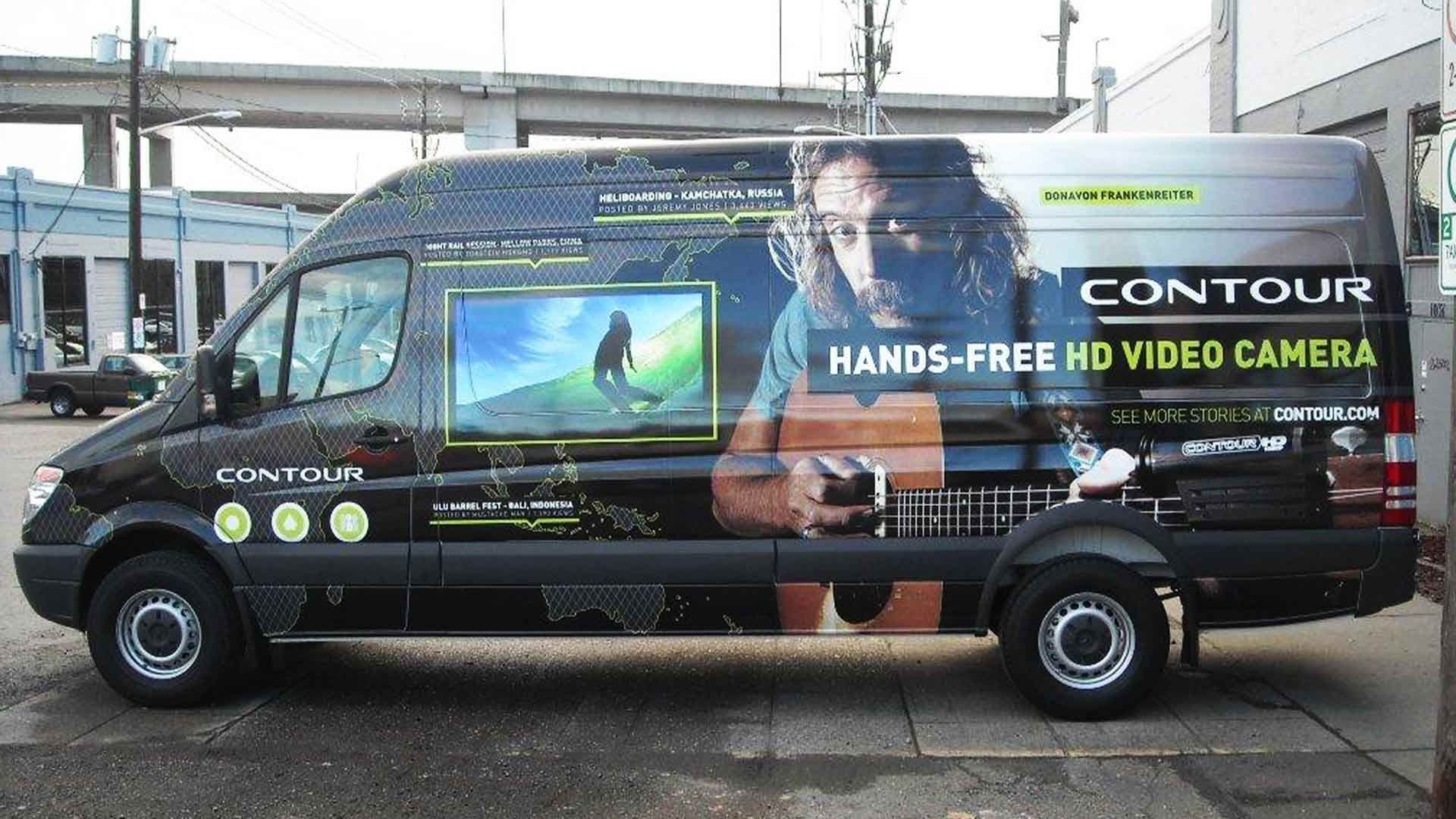 A black promotional van for Contour cameras, featuring a large screen on its side displaying an action sports video.