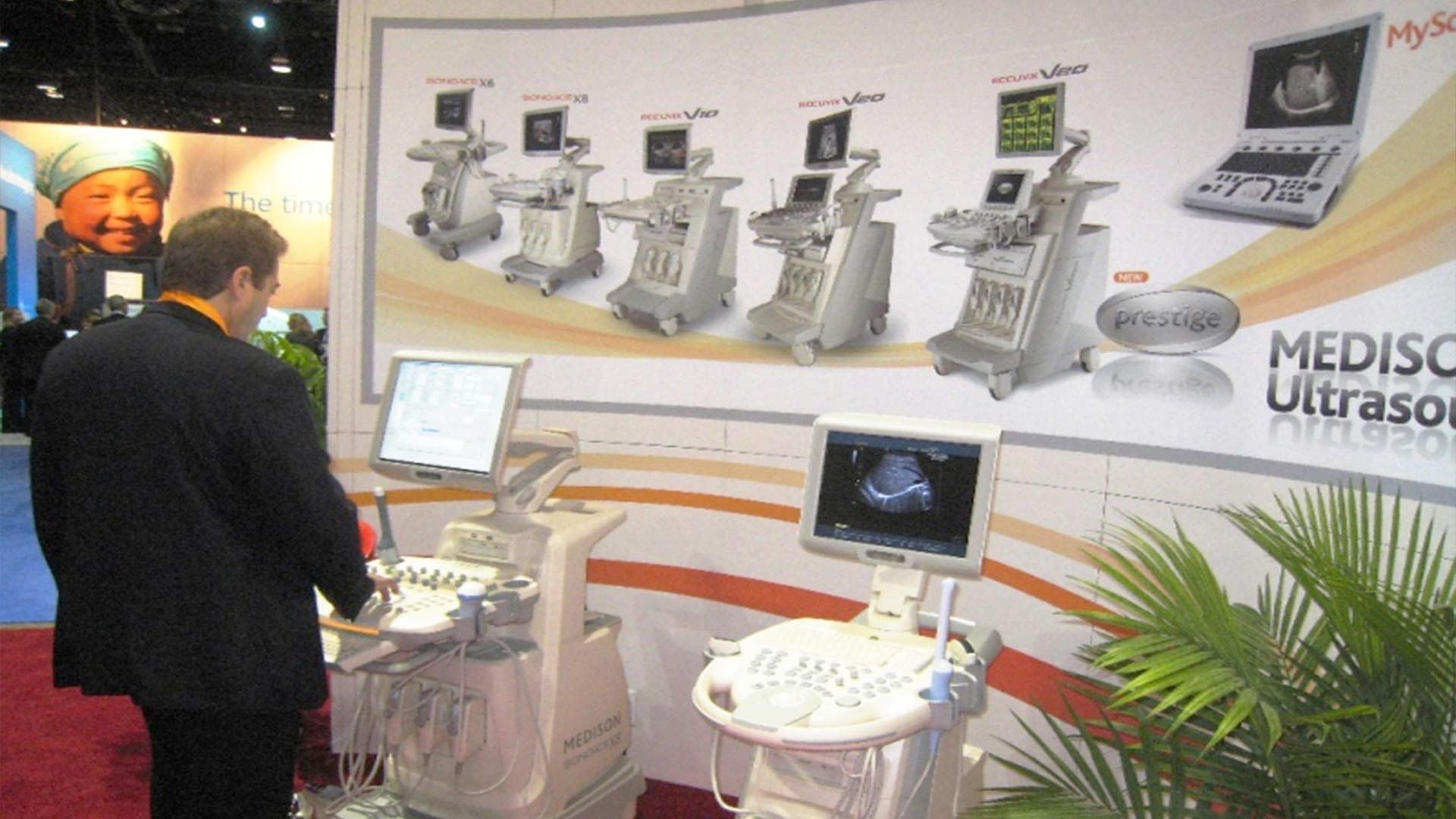 A person stands at a trade show booth featuring Medison ultrasound machines on display.