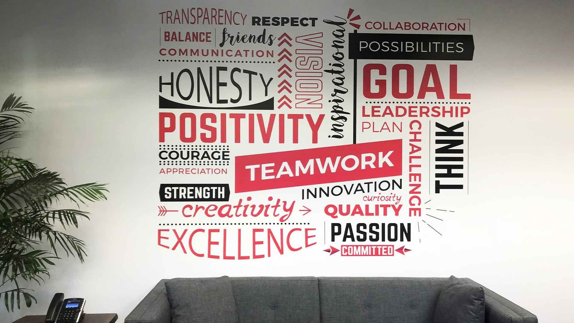 A wall decal featuring motivational words in red and black, displayed above a gray sofa in an office setting.