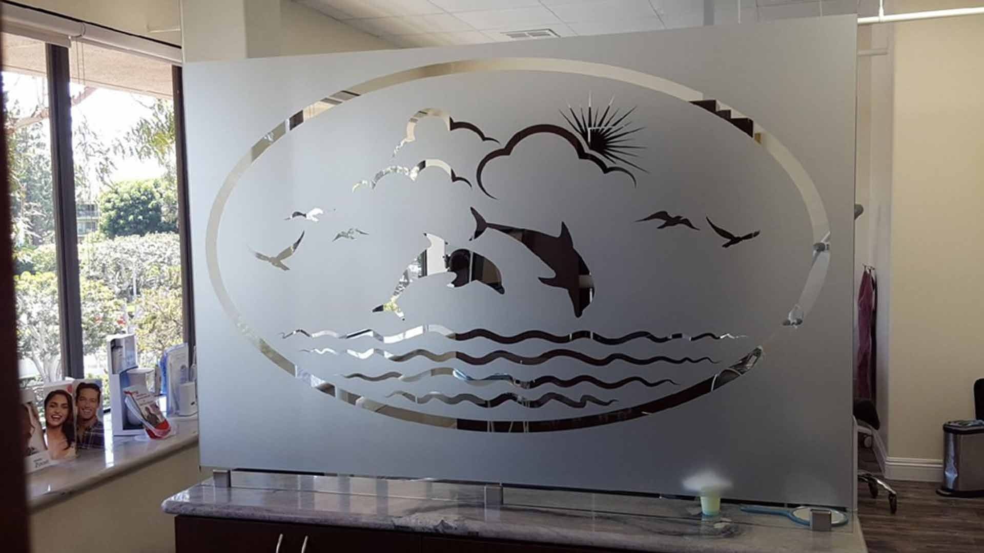 A frosted glass room divider featuring an oval cutout design of dolphins jumping in the ocean with clouds and birds.