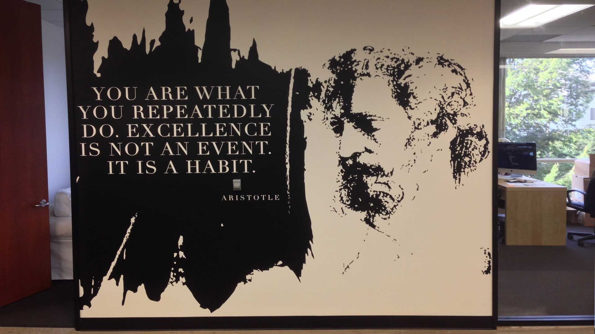 A wall decal in an office features a quote by Aristotle: 