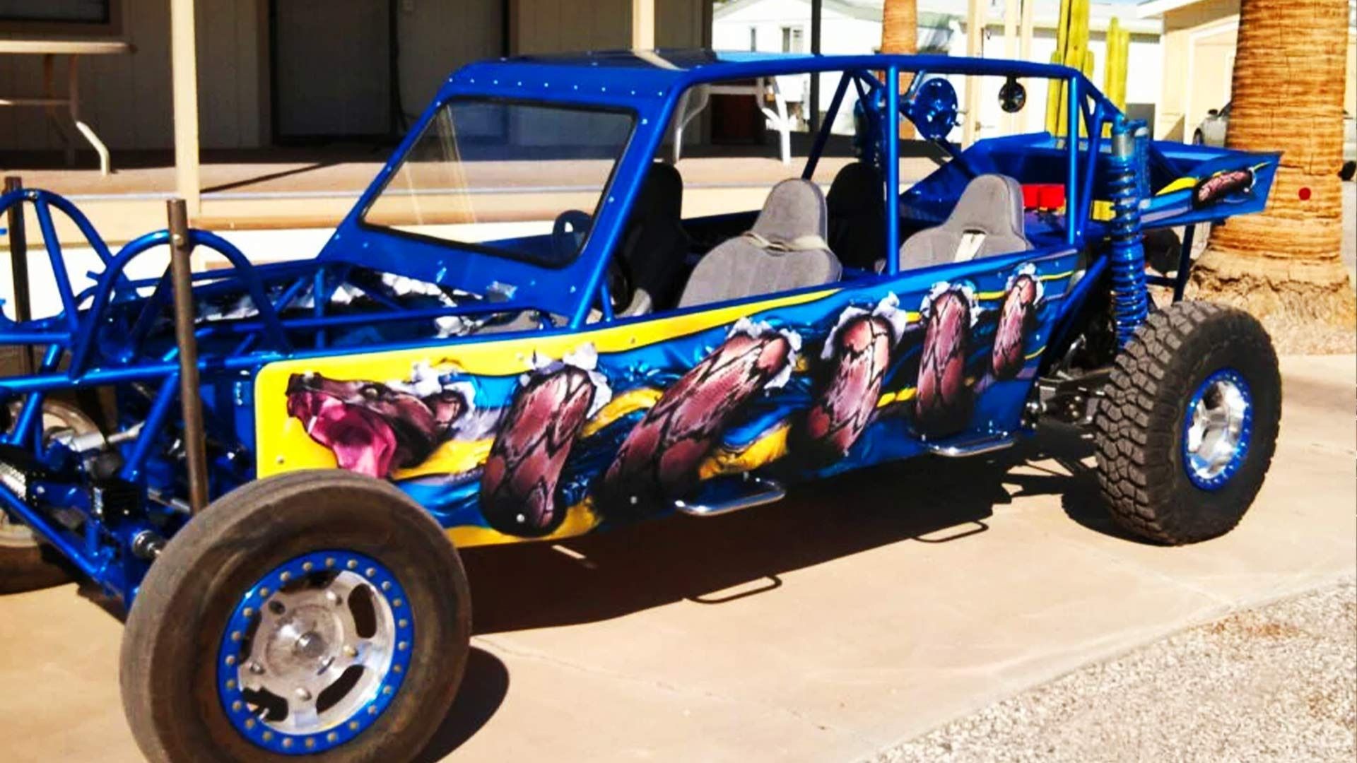 A bright blue custom sand rail vehicle with a vibrant, illustrated wrap showing multiple animal heads on its side.