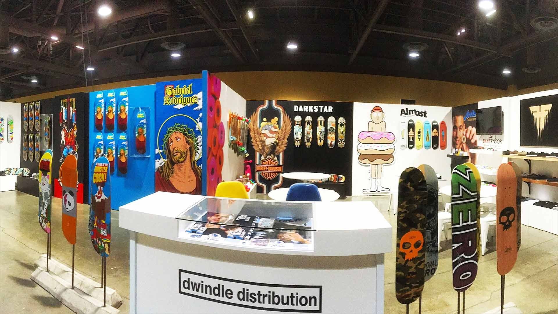 A Dwindle Distribution trade show booth displays various skateboard decks and graphics on blue, black, and white walls.