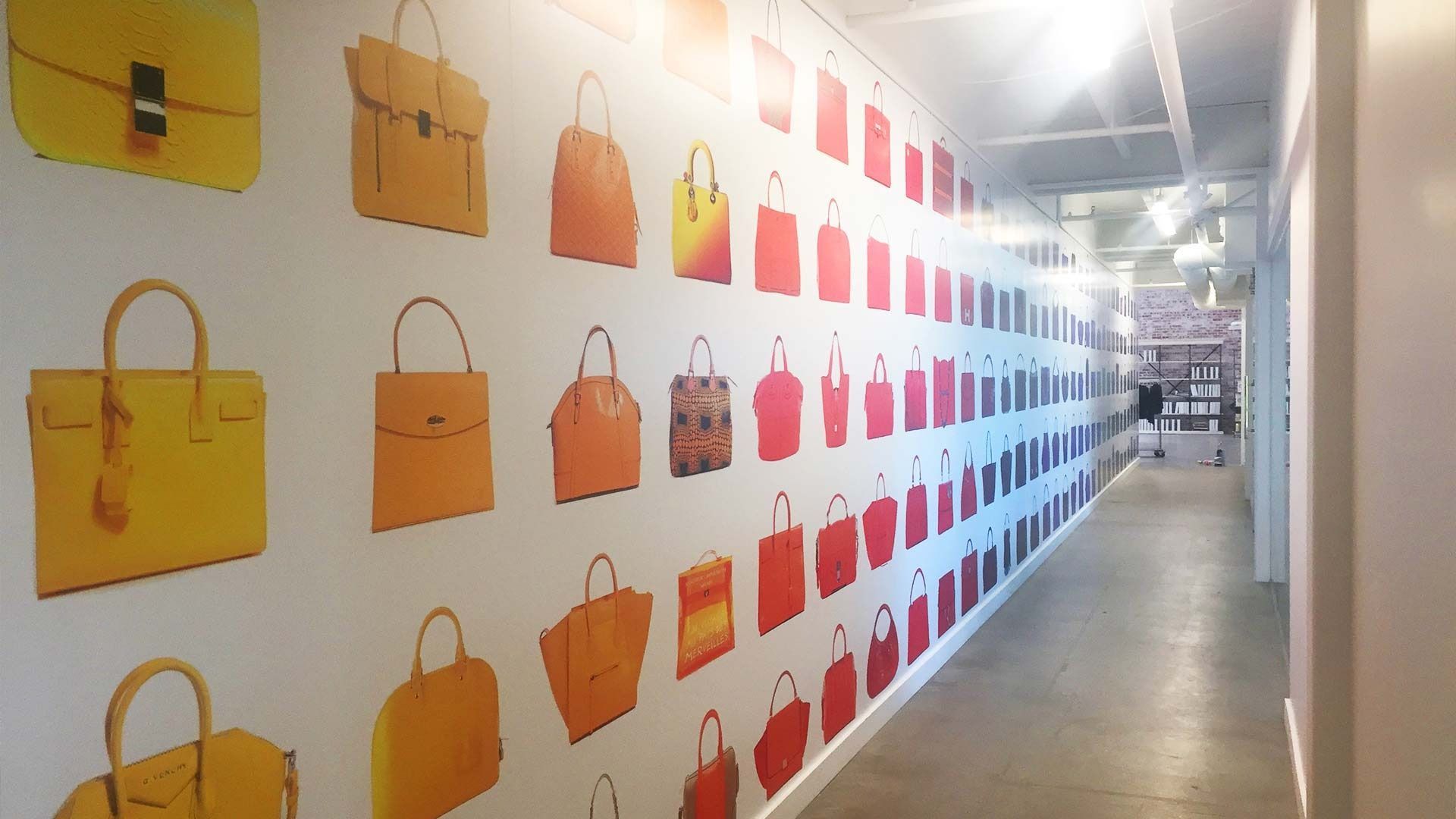 A hallway with a wall decorated with rows of handbag illustrations in a gradient from yellow to orange, red, and blue.