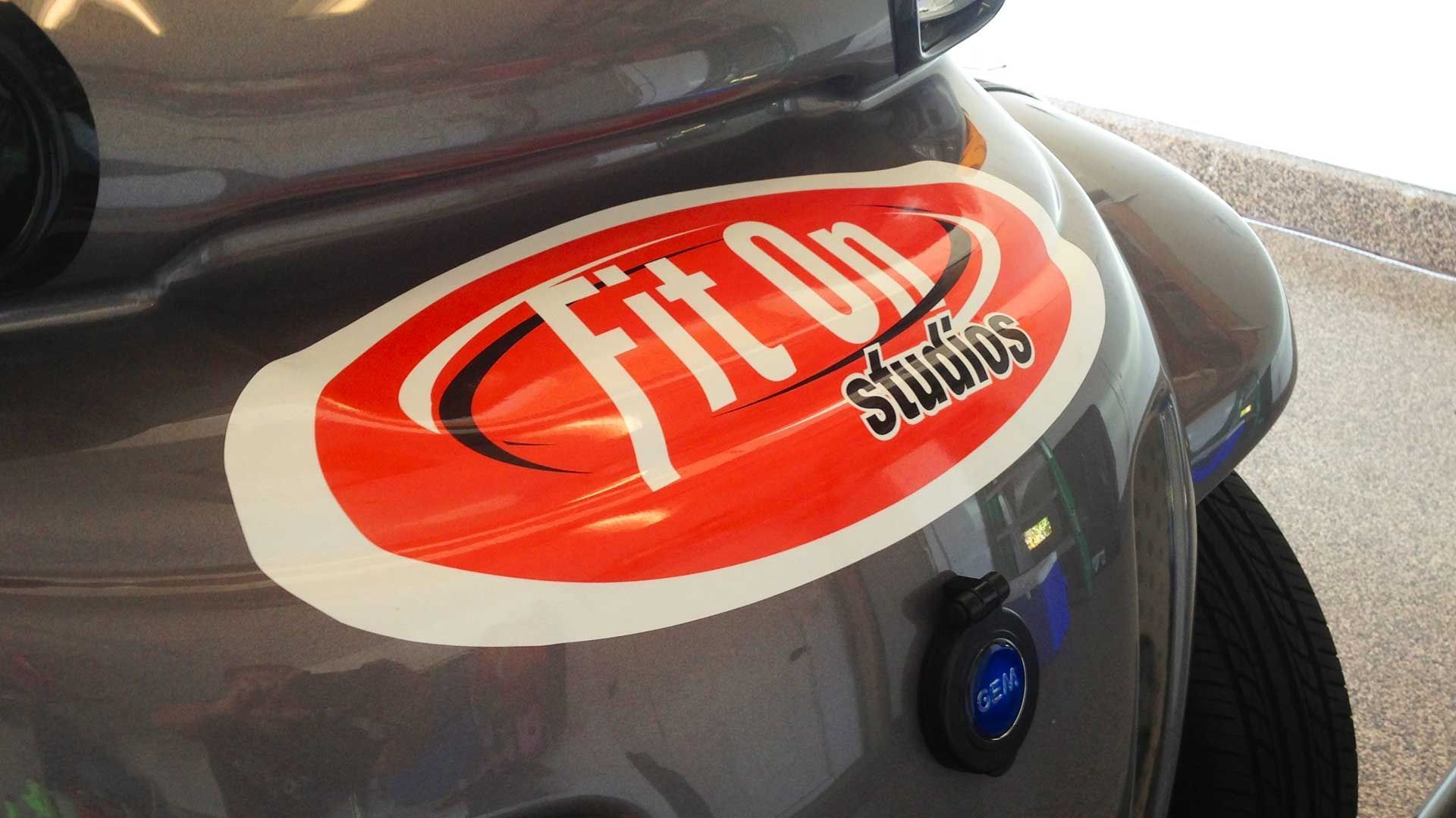 A red oval logo for FitOn Studios is prominently displayed on the side of a grey car.