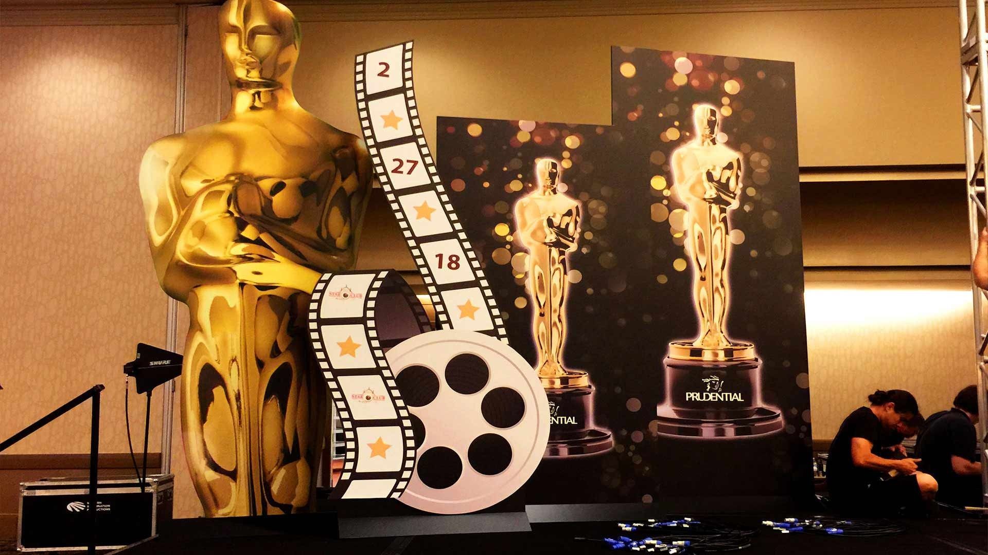 An Oscars-themed display with a large gold statue, film reel, and film strip standing on a stage.