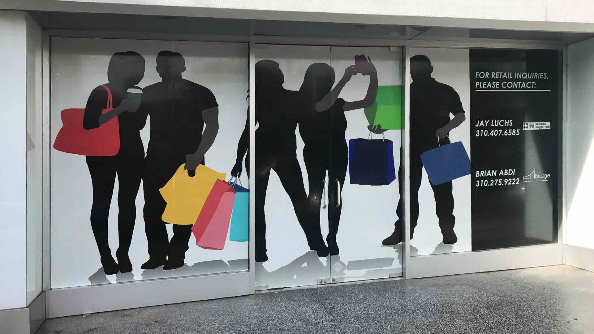 Store window graphic showing silhouettes of people carrying colorful shopping bags and a person taking a selfie.