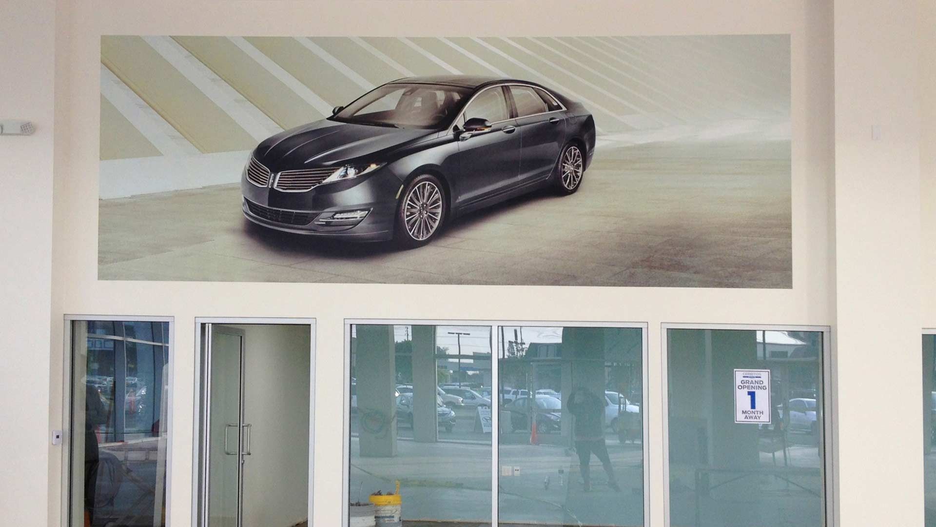 A wall decal featuring a dark gray Lincoln sedan above a series of glass windows and doors in an indoor setting.