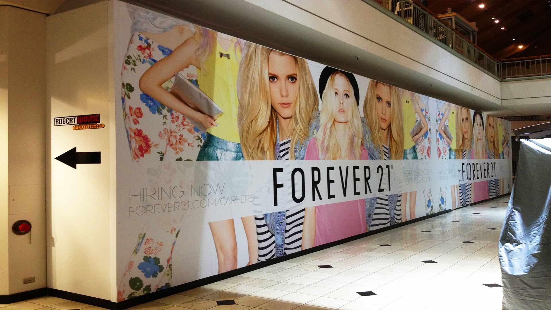 A long hoarding featuring advertisements for the clothing brand Forever 21, displayed in a shopping mall hallway.