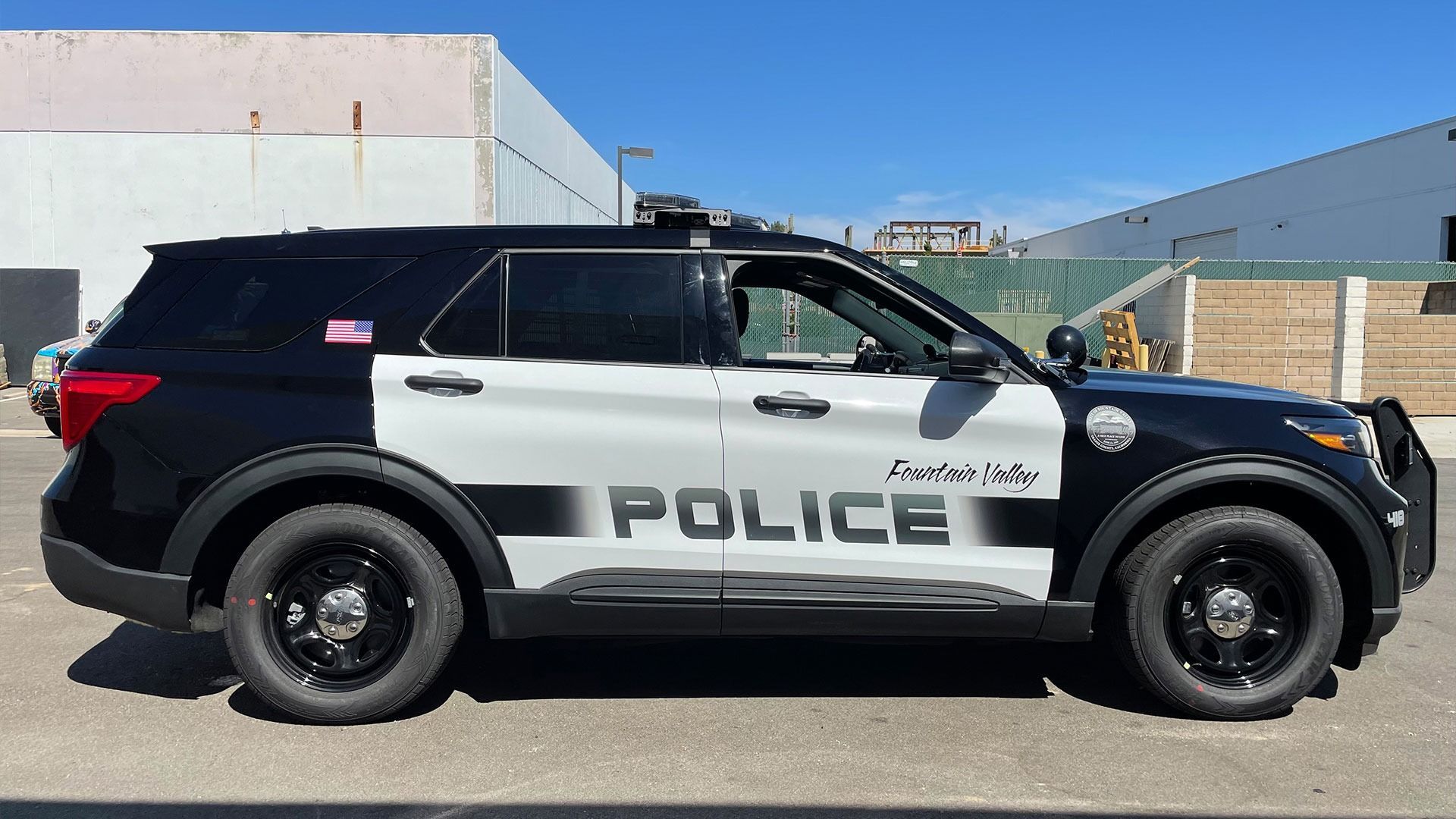 A black and white police SUV parked on an asphalt lot against a background of industrial buildings.
