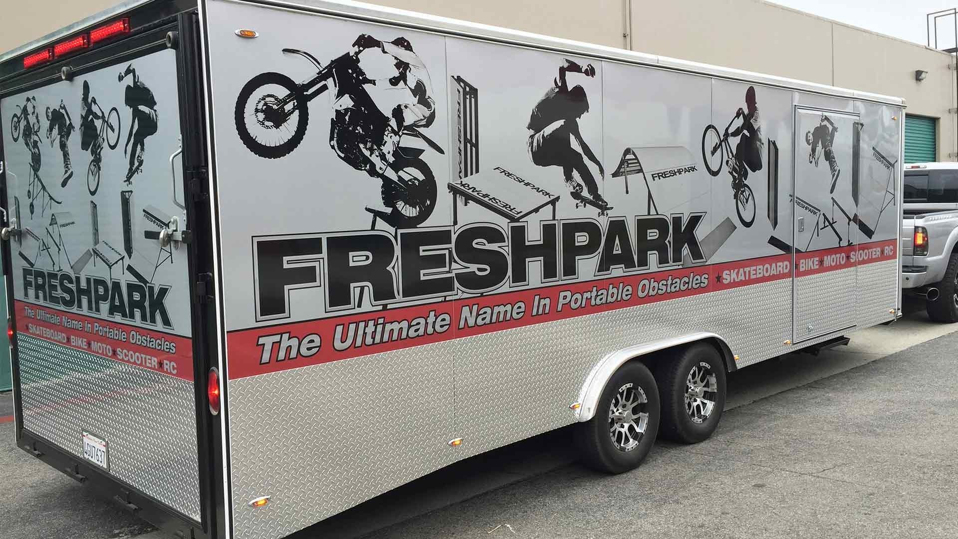 A branded Freshpark silver trailer parked outdoors, featuring action graphics of motocross and skateboarding silhouettes.