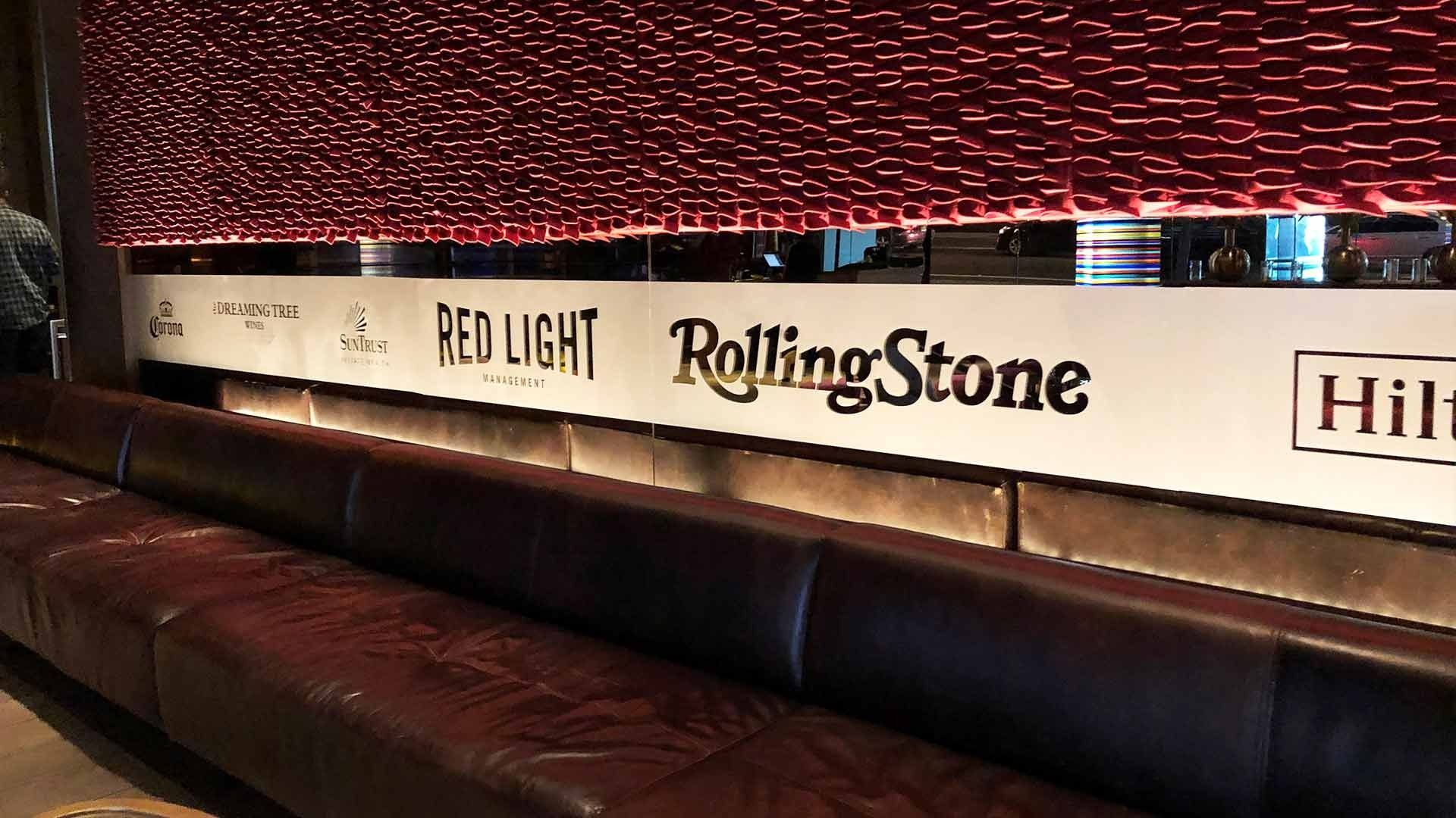 A long, dark leather bench sits below a white wall displaying logos for Red Light, Rolling Stone, and Hilton.