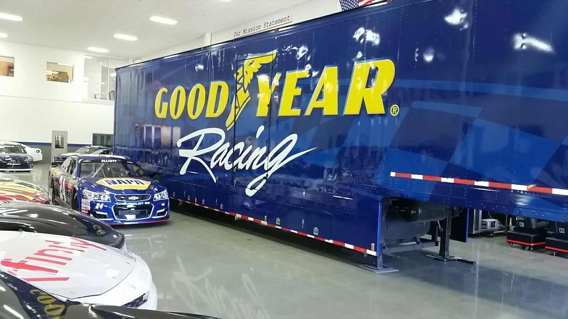 A blue Goodyear Racing trailer parked in a garage next to a race car.