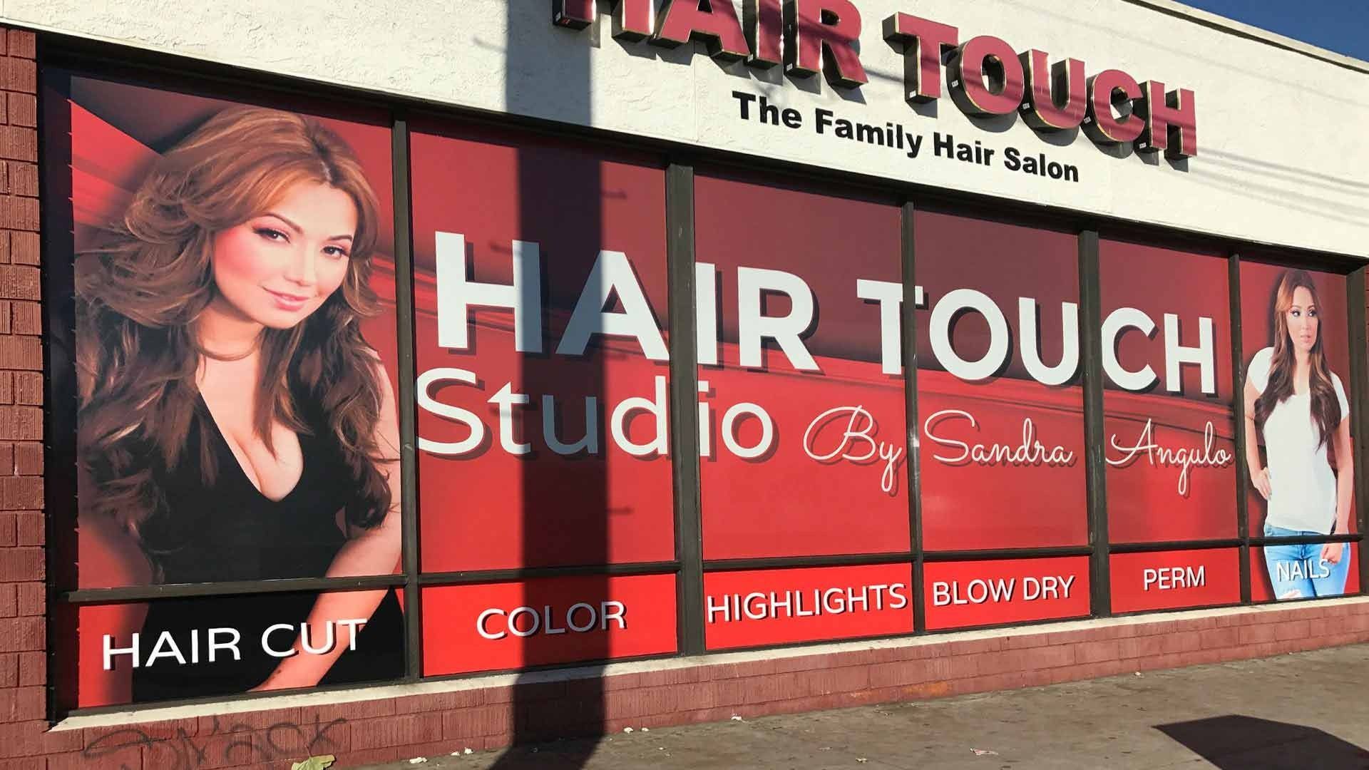 Storefront window of Hair Touch salon with large red advertisements, photos of two women, and a list of services.