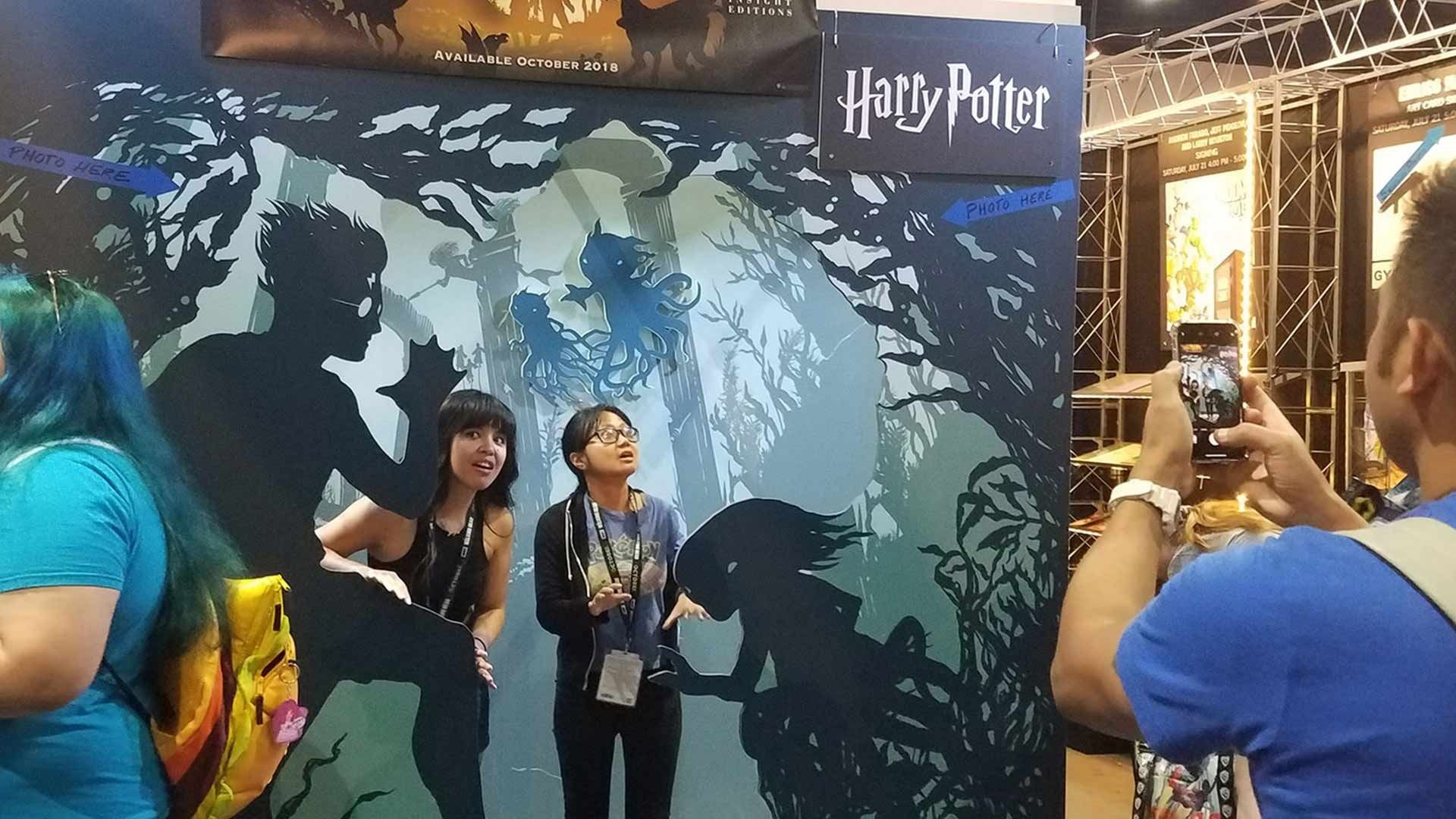 Two people stand for a photo in front of a Harry Potter display while a third person takes a picture of them.
