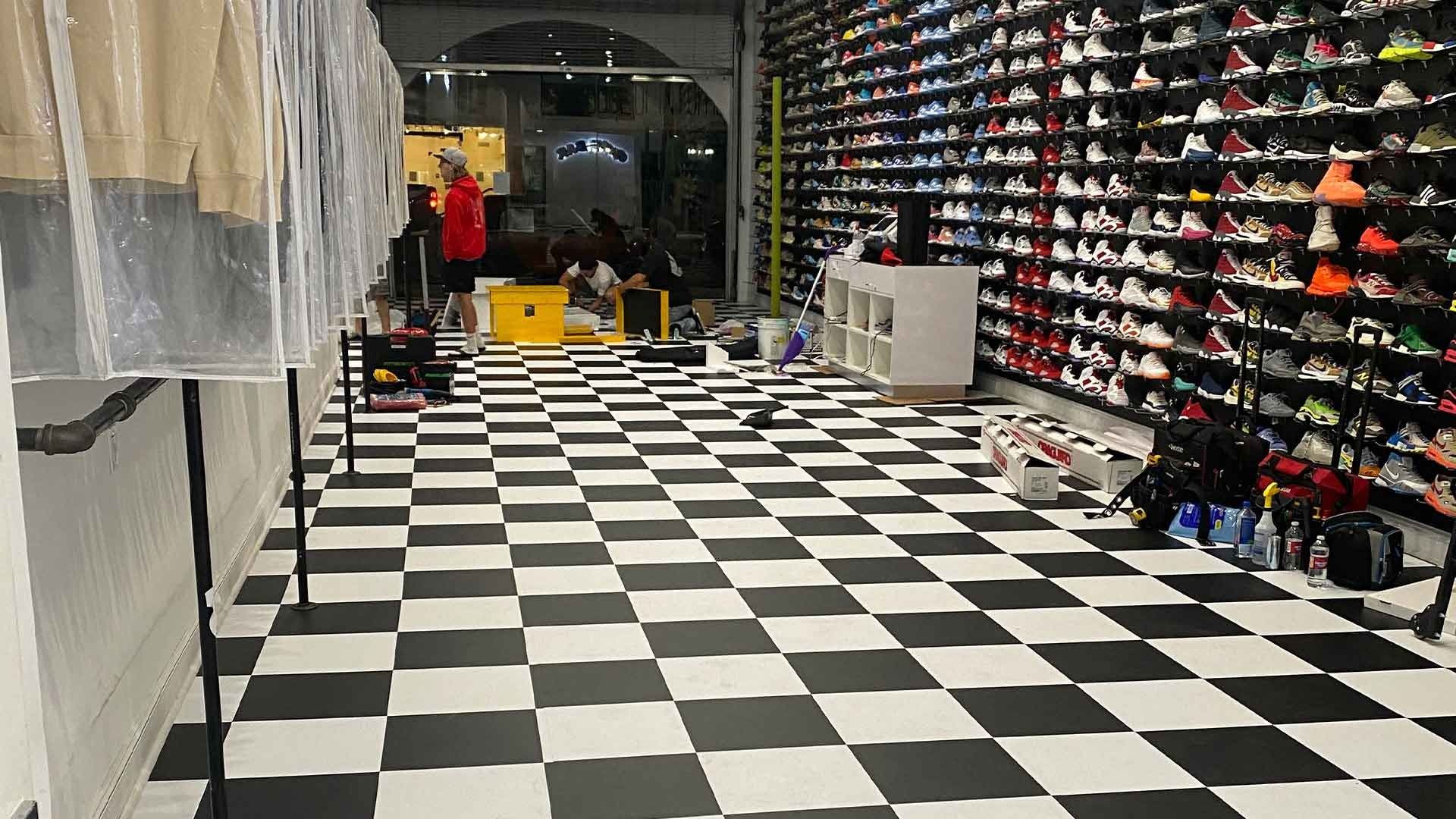 A retail store with a black-and-white checkered floor, shelves of sneakers, and clothing racks under protective covers.