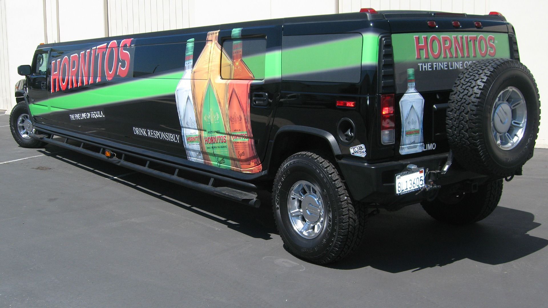 Black Hummer limousine parked outdoors, wrapped in a promotional design for Hornitos Tequila with imagery of bottles.