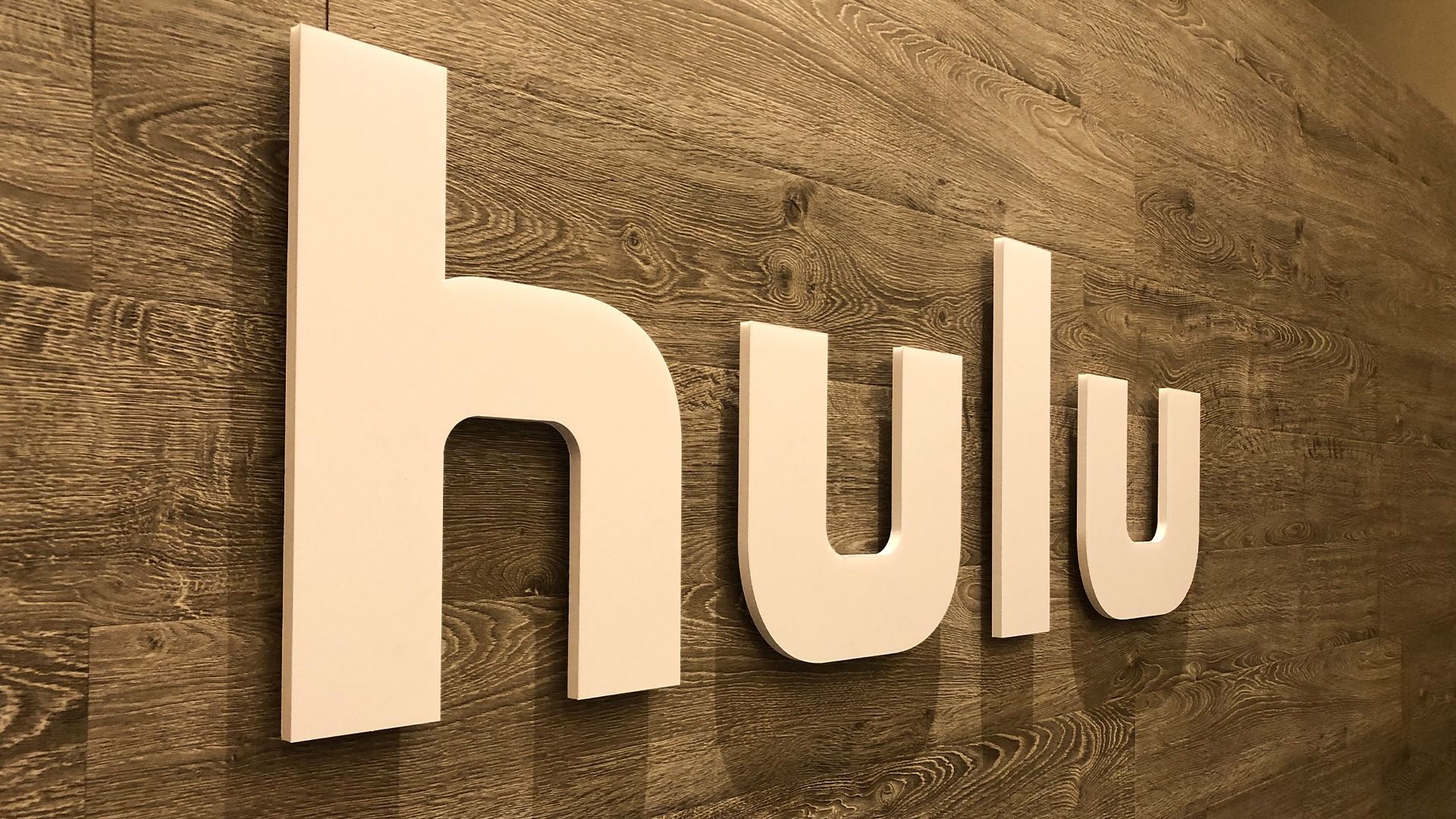A three-dimensional white Hulu logo mounted on a dark, textured wood-paneled wall.