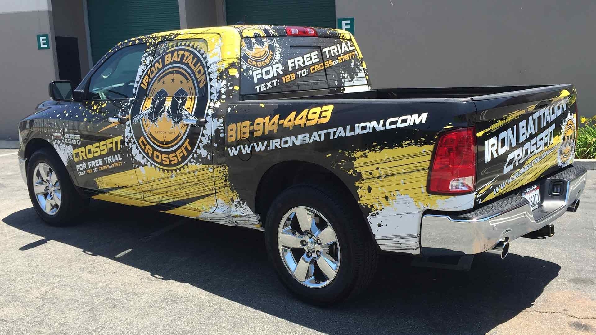 A black and yellow Iron Battalion CrossFit pickup truck parked on asphalt outside a building.