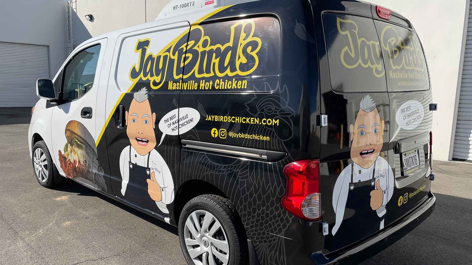 A Jay Bird's Chicken van parked outside, featuring a black-and-white wrap with a cartoon chef mascot.