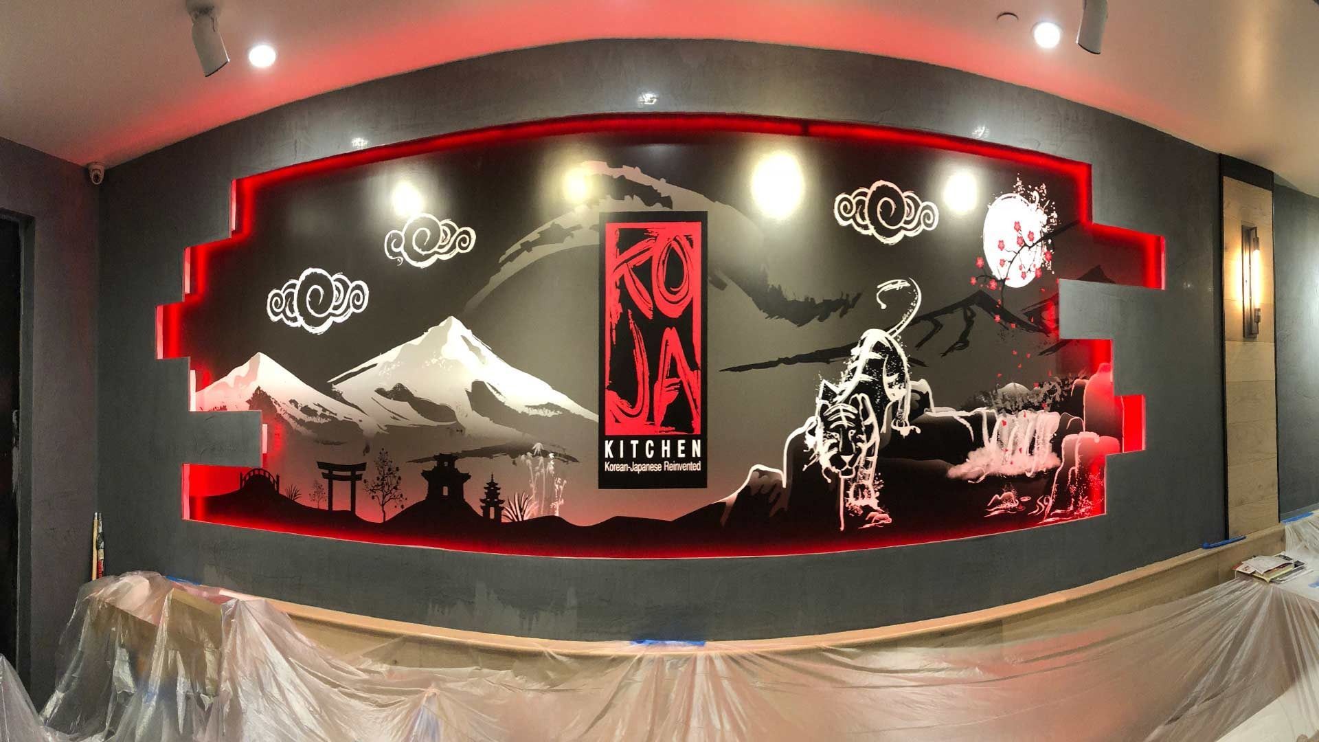 A mural featuring a central red logo, mountains, and a tiger silhouette, framed by recessed red lighting in a room.