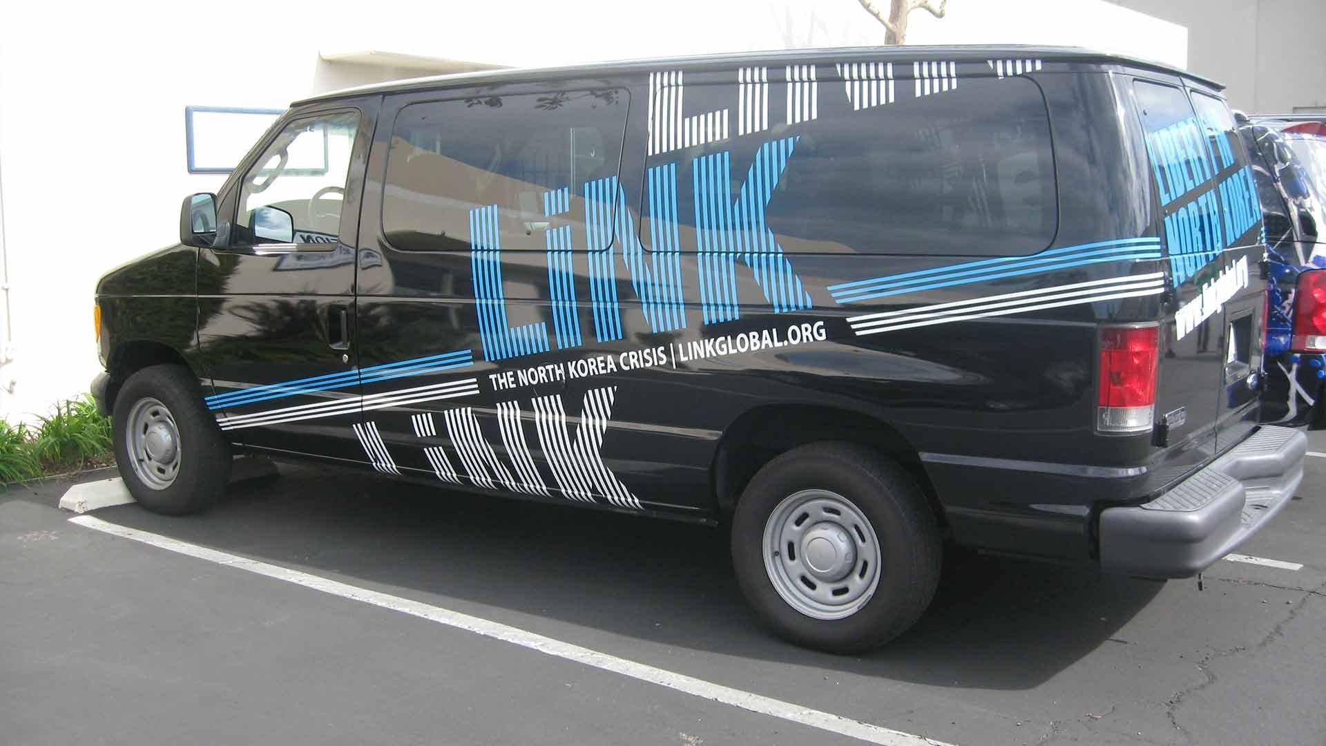 A black van parked in a lot, wrapped with blue and white 