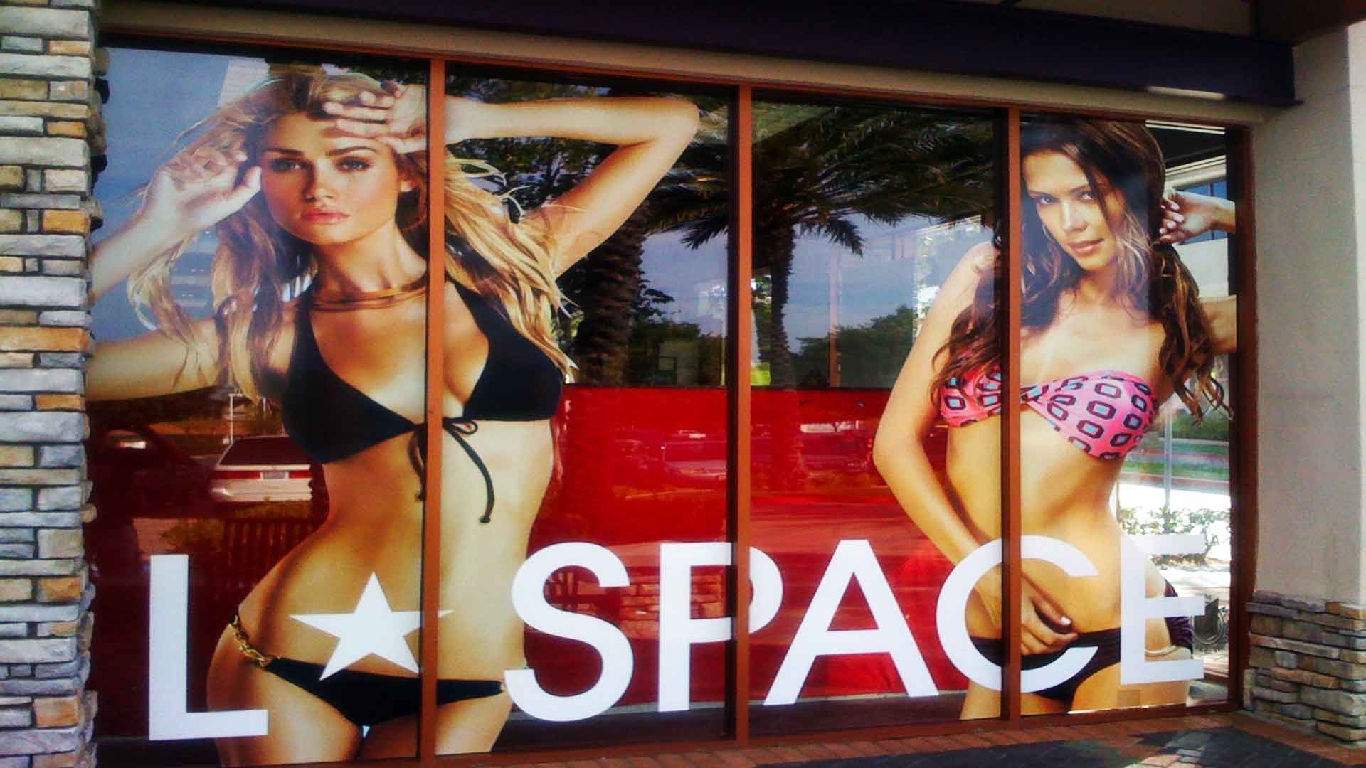 Storefront window display featuring two models in bikinis and the text 