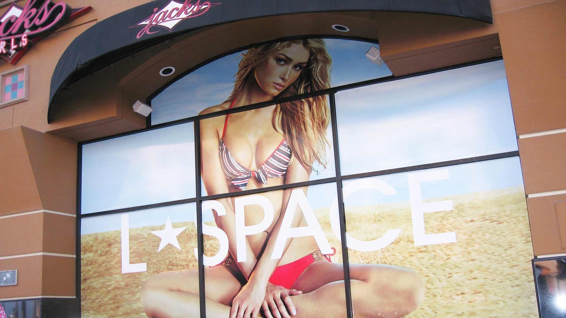 Storefront window decal featuring a woman in a bikini on a sandy beach with the text 