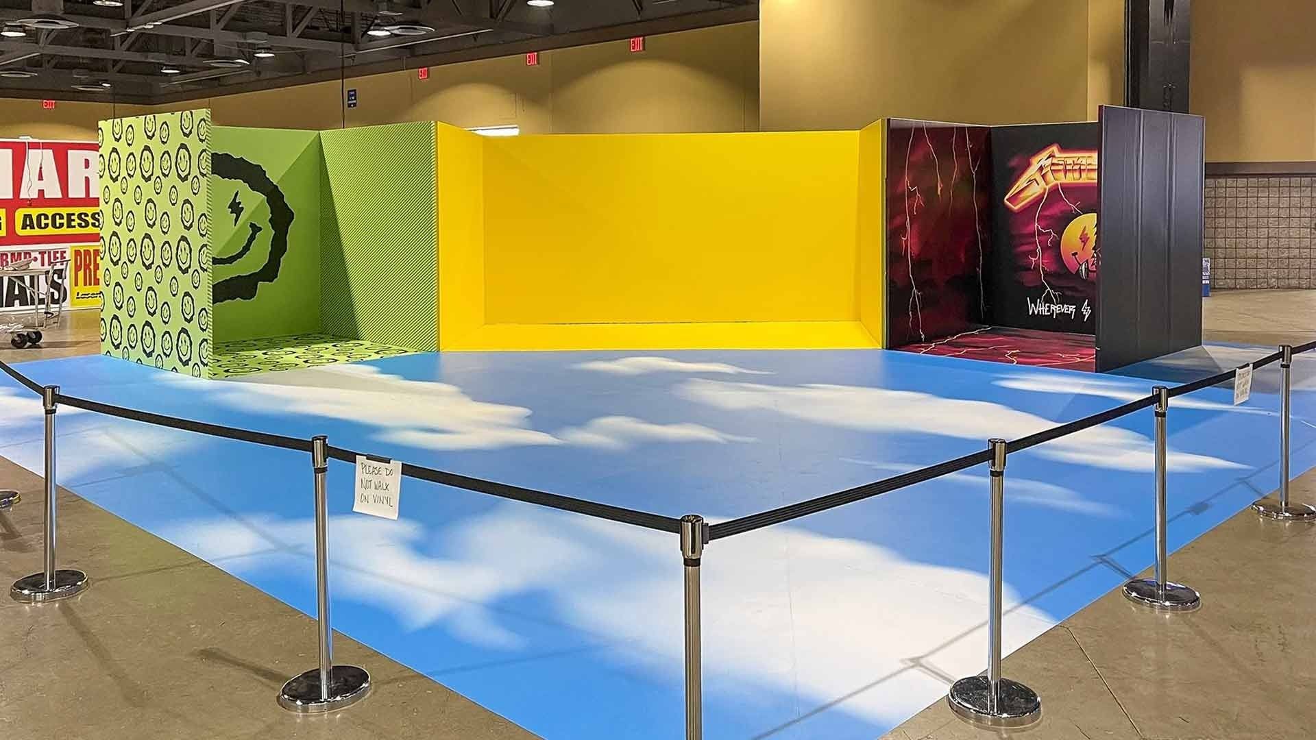 An empty photo booth area with a cloud-patterned floor and three distinct backdrop walls: green, yellow, and red.