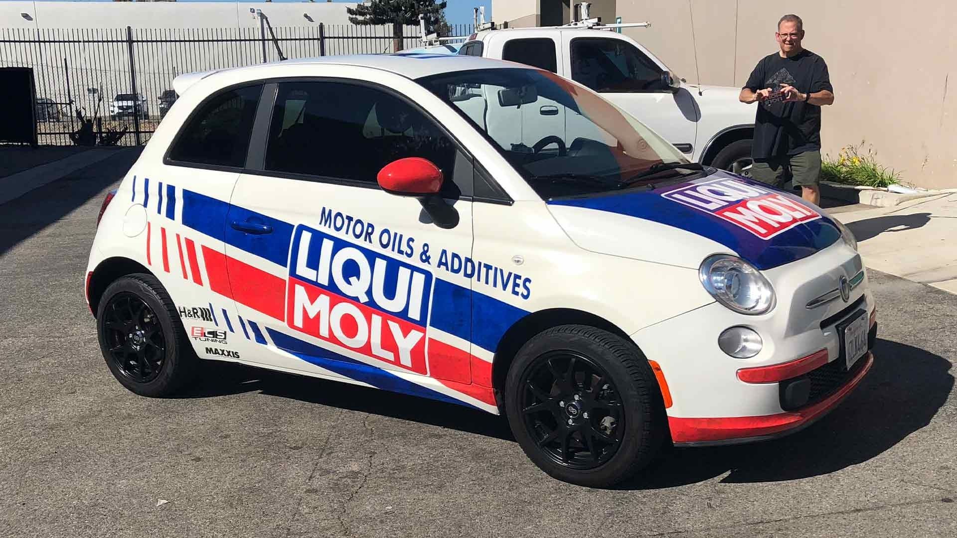 A white Fiat 500 branded with red and blue Liqui Moly decals parked outside near a man.