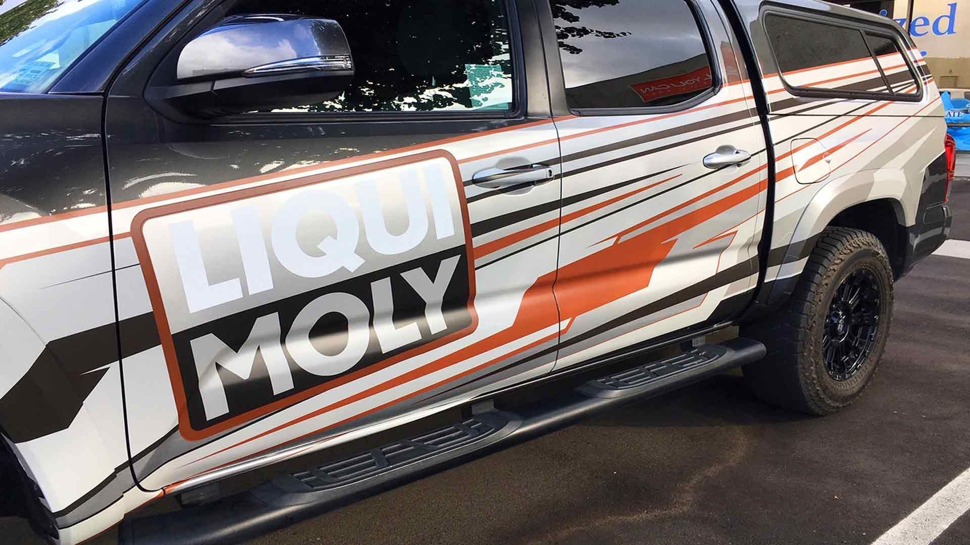 A dark gray and white pickup truck with orange racing decals and a prominent Liqui Moly logo on the side.