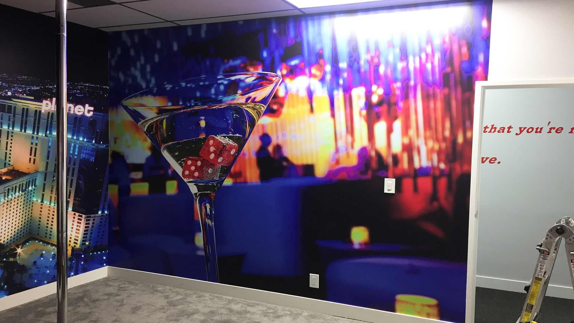 A wall mural in a room showing a large martini glass filled with dice against a vibrant blue and red lounge background.