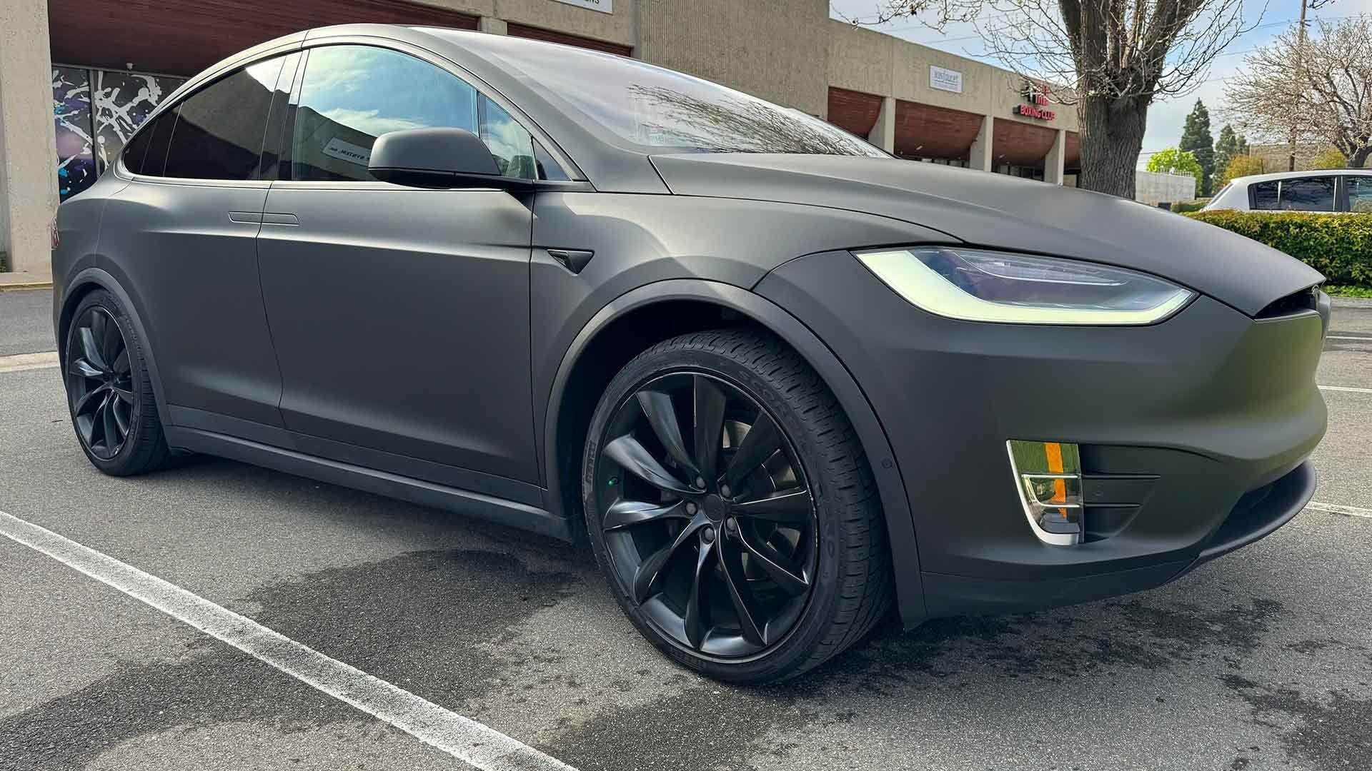 A matte black Tesla Model X parked in an outdoor lot on a sunny day.