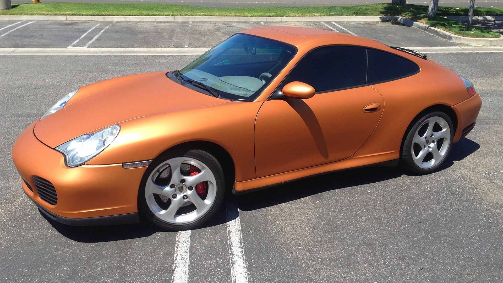 A matte copper Porsche 911 coupe parked in an asphalt parking lot on a sunny day.