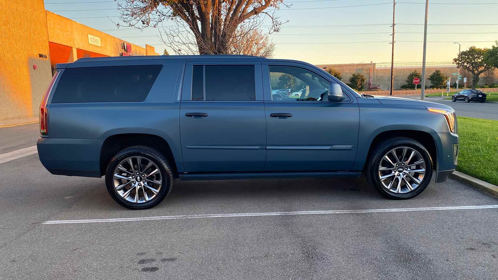 A matte blue Cadillac Escalade SUV parked in an outdoor parking lot at dusk.