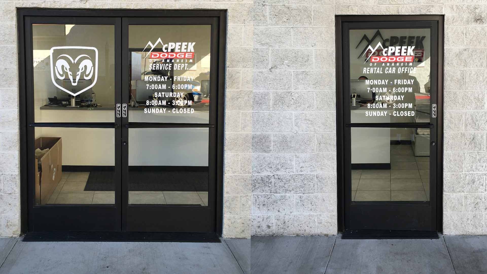 Two black-framed glass commercial entryways, one double and one single, with business hours and logos on the glass.