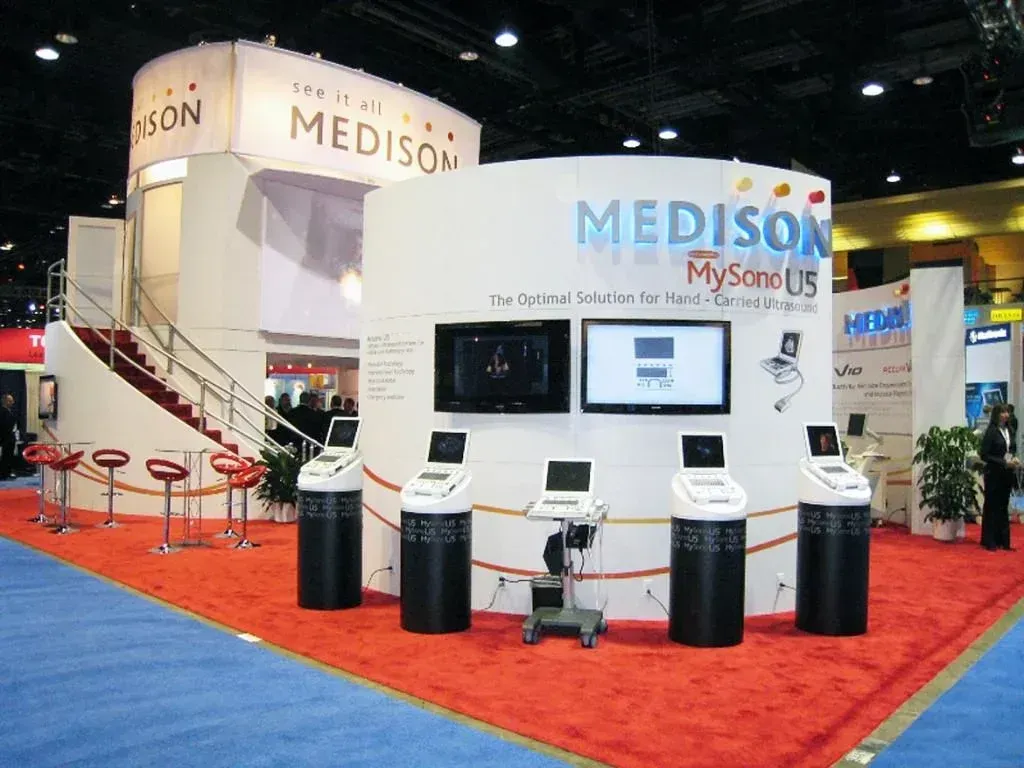 Medison trade show booth with several medical ultrasound diagnostic machines on display against a large white curved wall.