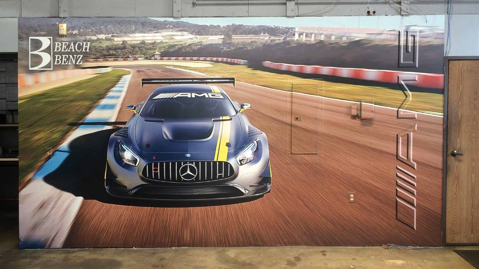 A blue Mercedes-AMG race car with a yellow stripe on a racetrack, with branding on the wall display.